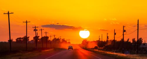 A truck driving down a road flanked by electric utility lines and transformers as the sun sets